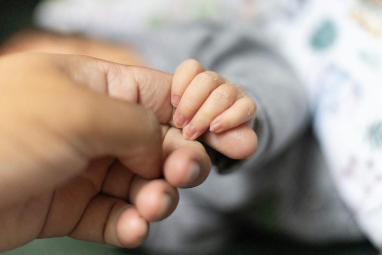 Tender moment of a baby hand holding an adult's finger, symbolizing bond.